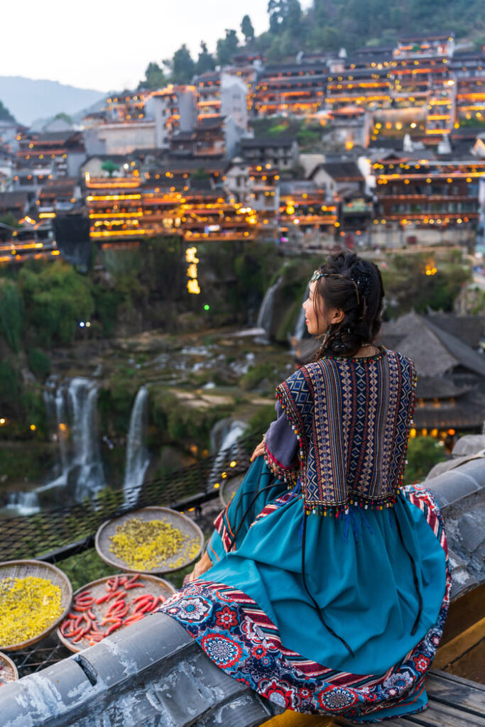 Mujer de China, con una cascada de fondo, y casas de madera sobre pilote.
