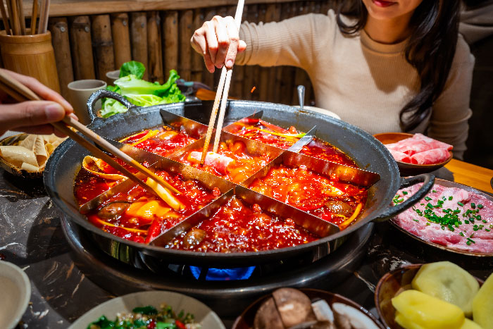 Una mujer sentada en una mesa de restaurante, probando una tipica comida china con palillos