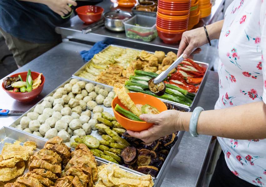 Una persona sirviéndose verduras que estan en una charola.