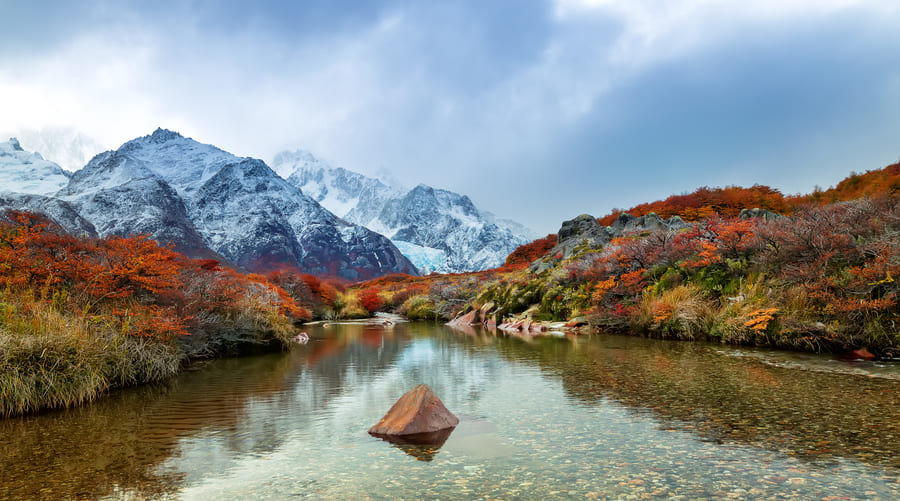 un río rodeado de montañas con un follaje de varios colores en otoño